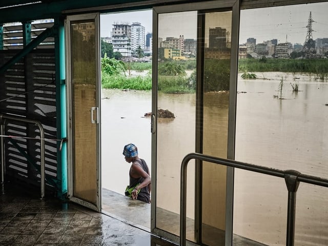 Frau watet durch hüfthohes Wasser zu einem Gebäude