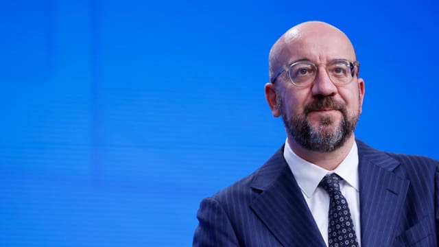 Charles Michel trägt eine Brille und einen Anzug. Er steht vor einem blauen Hintergrund.