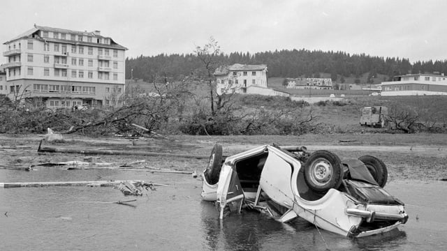 Eine verwüstete Landschaft. Im Vordergrund ein zerstörtes Auto auf dem Dach liegend.