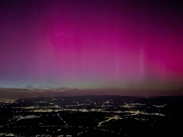 Nordlichter über einer nächtlichen Stadtlandschaft.