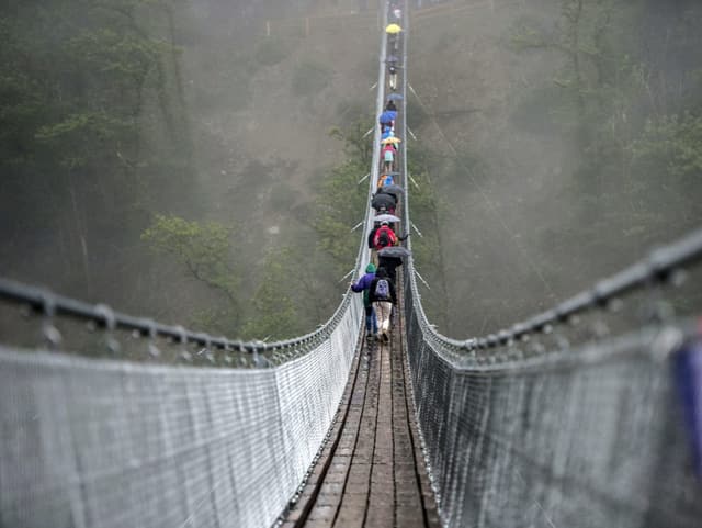 Hängebrücke und Wanderer mit Regenschirme.