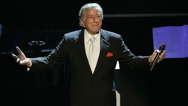 Tony Bennett steht mit einem Mikrofon und ausgebreiteten Armen auf der Bühne.