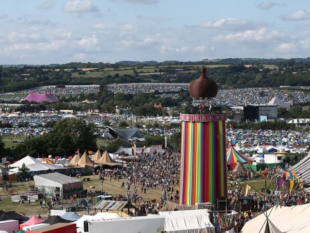 Überblick über ein Musikfestivalgelände mit einem bunten Turm und Zelten.