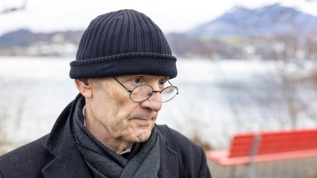 Man mit Brille und schwarzer Kappe vor einem See.