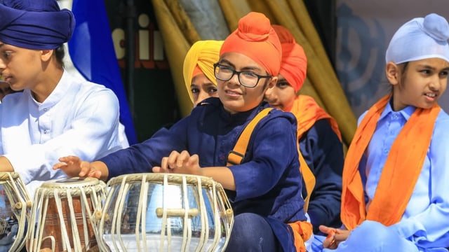 Farbenfroh gekleidete Kinder mit Sikh-Kopfbedeckungen und Trommeln