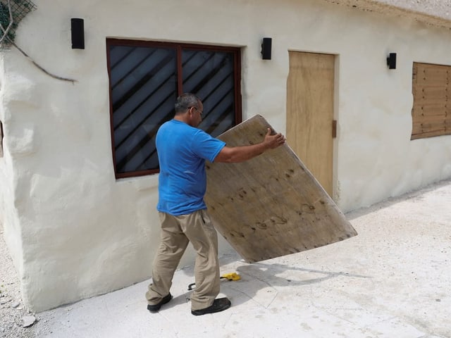 Mann befestigt Holzplatten an Fenstern eines Gebäudes.