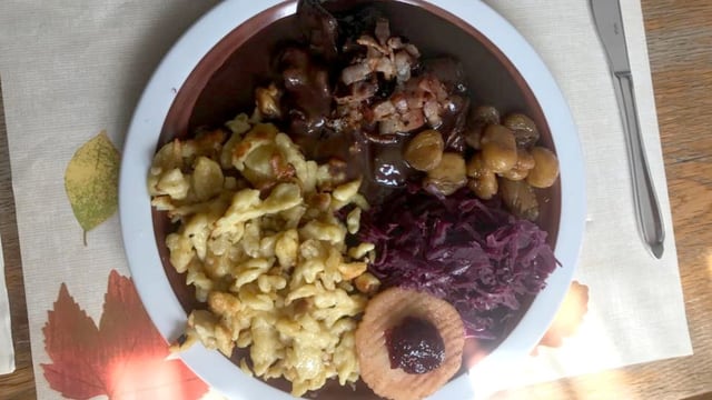 Rehpfeffer mit Spätzli und Rotkraut auf einem Teller.