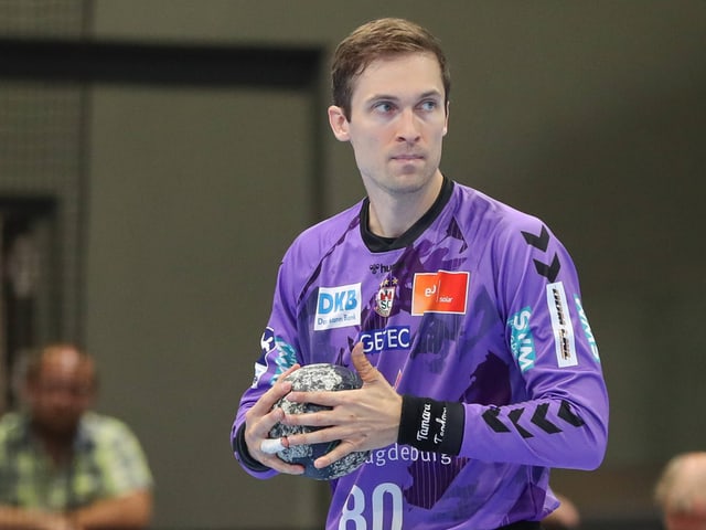 Handballspieler im lila Trikot hält einen Ball.