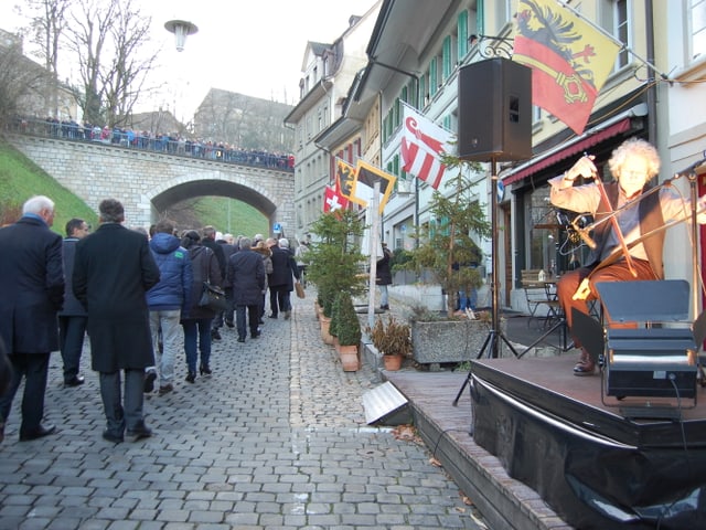 Leute gehen die Gasse hoch, jemand spielt Cello.