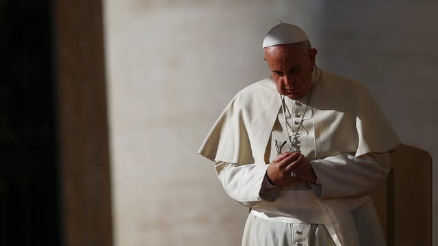 Aufnahme von Papst Franziskus mit gefalteten Händen und gesenktem Kopf.