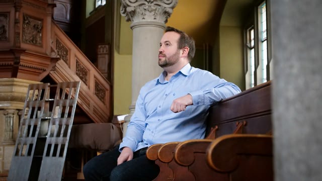 Renato Pfeffer sitzt in einer Kirche. Er trägt ein blaues Hemd.