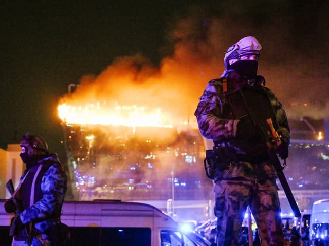 Sicherheitskräfte vor brennendem Gebäude.