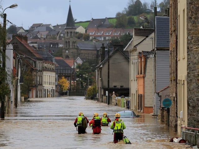 Feuerwehrleute schreiten durch die Wassermassen auf einer überfluteten Strasse.