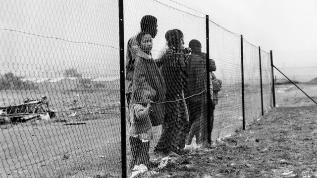 Dunkelhäutige Menschen vor Grenzzaun in Johannesburg, der sie von Siedlungen der weissen Bevölkerung trennt.