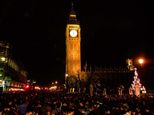 Menschenmenge vor Turm mit Uhr. Es ist Dunkel.