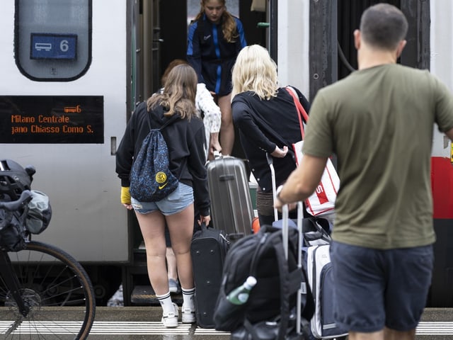 Menschen steigen mit Gepäck in einen Zug ein.