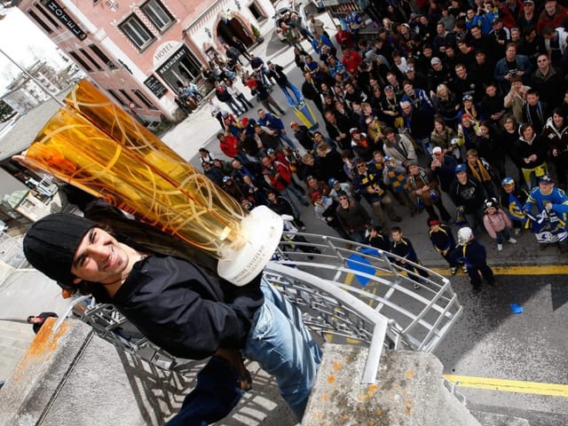 Person mit grossem Pokal vor einer Menschenmenge auf dem Balkon stehend.