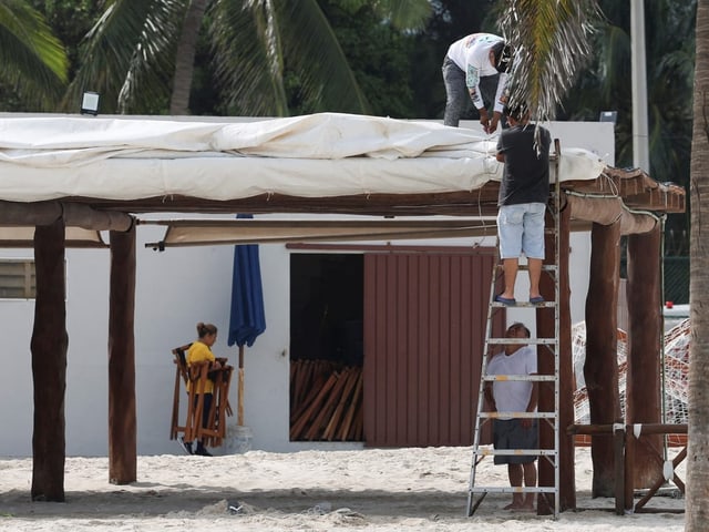 Zwei Männer auf Leiter reparieren Strandbar-Dach.