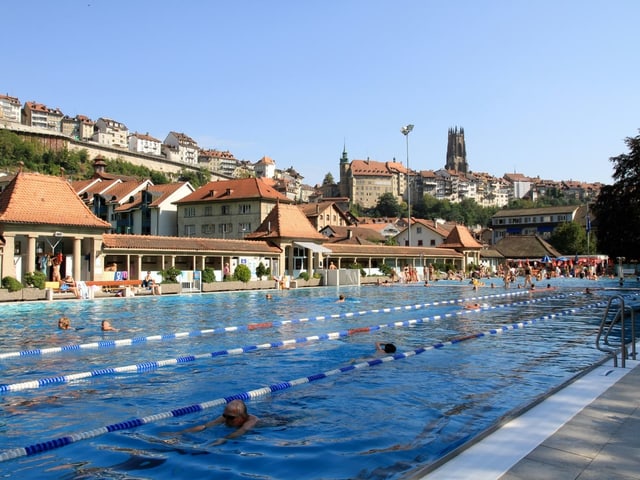 Schwimmbad vor malerischer Stadtansicht mit Turm und Häusern.