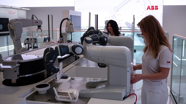 Zwei Frauen stehen neben Robotern auf dem Messestand der Firma ABB auf der Hannover Messe.