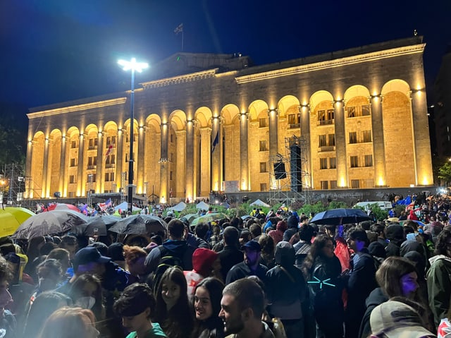 Menschenmenge vor beleuchtetem Gebäude bei Nacht.