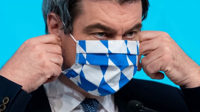 Markus Söder zieht sich eine Hygienemaske an