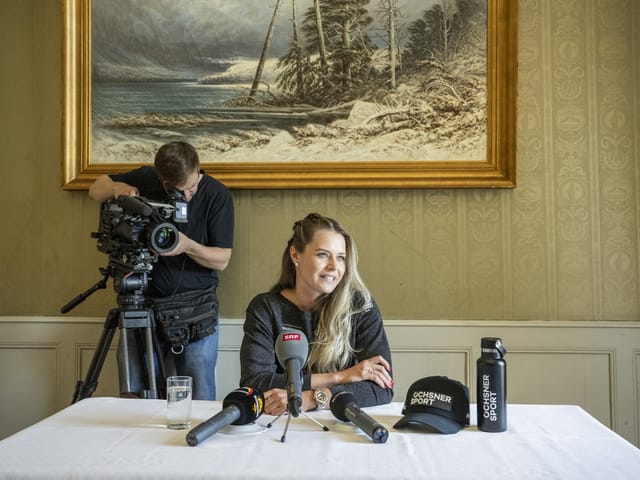 Frau bei Pressekonferenz mit Kameramann im Hintergrund.