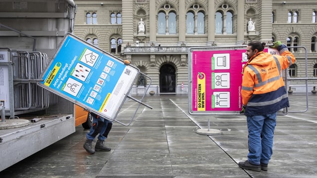 Arbeiter tragen Tafeln mit Covid-Massnahmen vor dem Bundeshaus