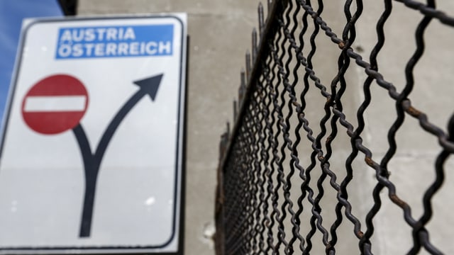 Ein Strassenschild steht an einer Hausmauer neben einem schwarzen Zaun.