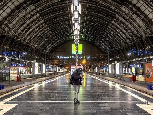 Ein Mann schaut am Gleis auf sein Smartphone.