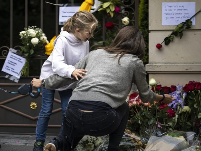 Die Frau ist in Begleitung ihrer Tochter, viele Blumen an Tor und auf Boden.