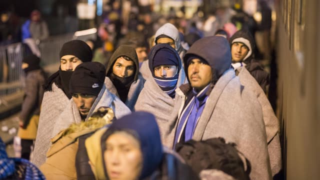 Junge Männer stehen nachts in Wolldecken gehüllt auf einem Bahnsteig.