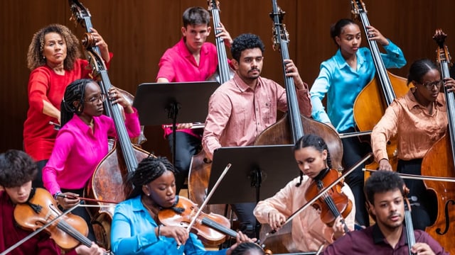 Orchester mit Menschen verschiedener Hautfarbe in bunter Kleidung.