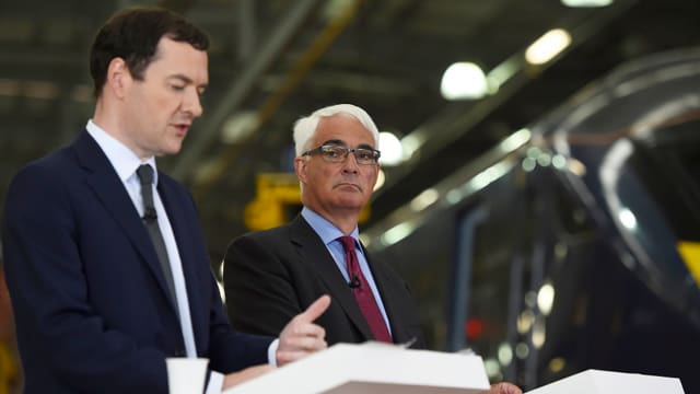 Osborne und Darling sprechen an zwei weissen Rednerpulten in der Halle einer Zugfabrik.