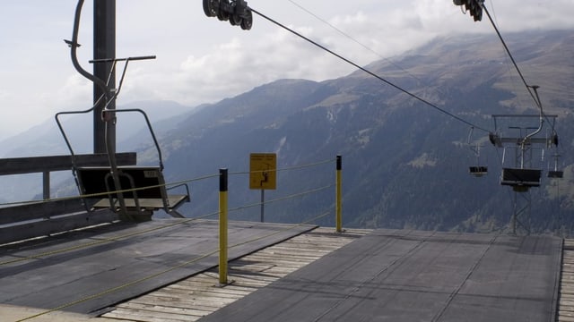 Zwei leere Sessellifte, im Hintergrund ist eine Bergspitze zu sehen.