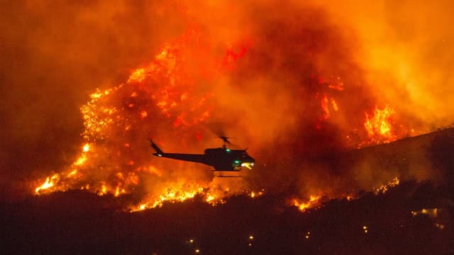 The helicopter circles over the forest fires. 