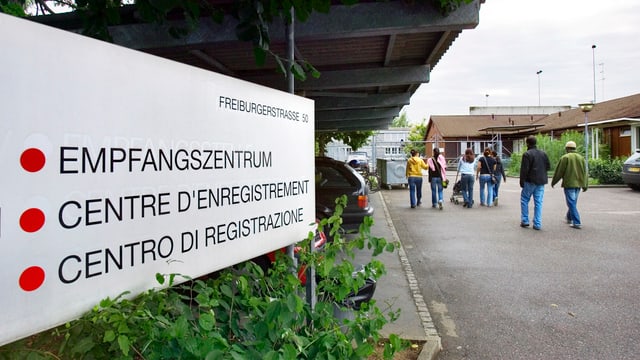 Menschen gehen an einem Empfangszentrums-Schild vorbei Richtung Eingang.