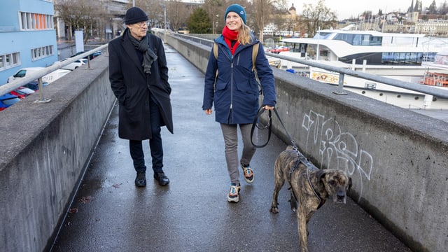 Mann und Frau spazieren über einen Steg, sie hält einen Hund an der Leine.