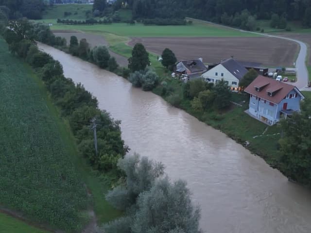 Fluss fliesst neben Wohnhäusern und Feldern.