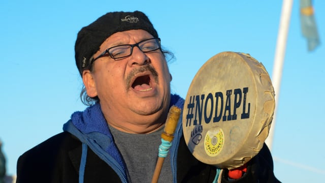 Ein Demonstrant schlägt ein Tamburin, auf dem #NODAPL steht.