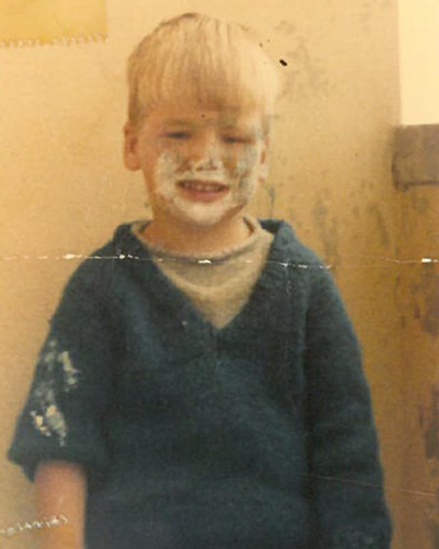 Ein blonder Junge mit einem verschmierten Gesicht und weissen Flecken auf seinem dunklen Pullover.