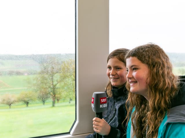 Zwei Kinder sitzen im Tram und sprechen ins Mikrofon.