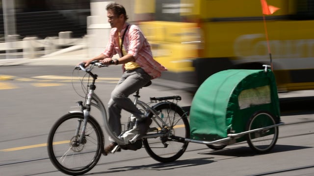 Mann fährt ein Elektrobike mit einem Kinderanhänger.