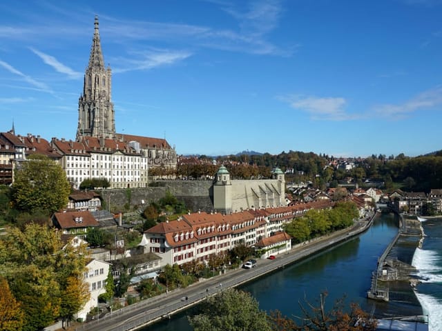 Panoramablick auf die Altstadt von Bern mit der Aare bei leicht bewölktem Himmel.