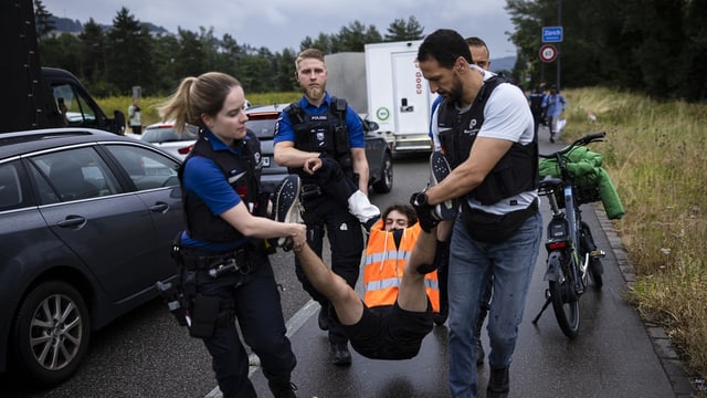 Vier Angestellte der Polizei tragen einen Klimakleber weg.