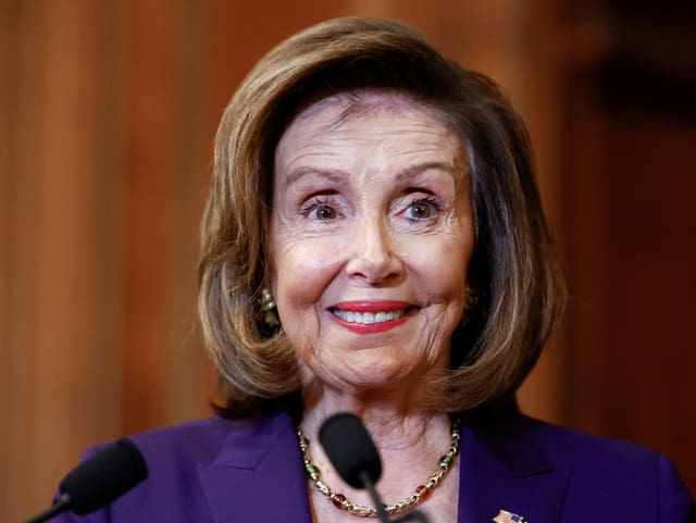 Pelosi vor einem Mikrophon, lächelnd.