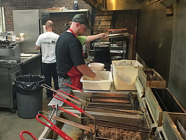 Ein Koch paniert Fisch, im Vordgrund Gitterkörbe in den Friteusen.