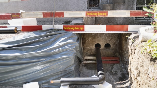 Fernwärmebaustelle mit Graben, schwarzen Rohren und Abschrankung.