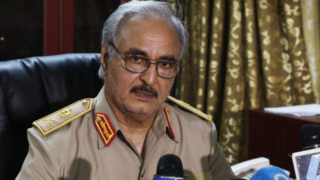 Haftar sitzt in seiner Generalsuniform vor mehreren Mikrofonen und blickt in die Kamera.