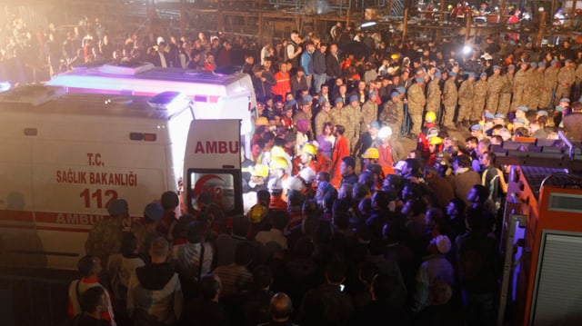 Zahlreiche Menschen auf Platz stehend, Ambulanz-Fahrzeuge